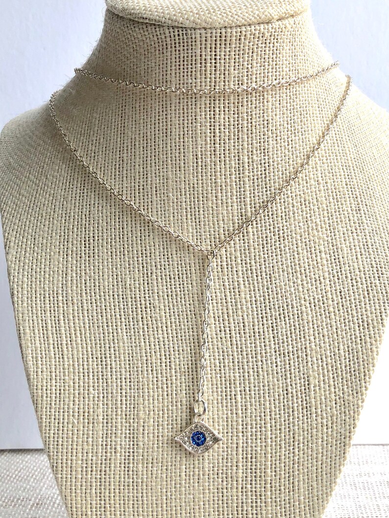 May include: A silver chain necklace with a blue evil eye charm. The charm is set with clear rhinestones and has a blue center.