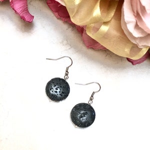 以下が含まれることがあります： 黒い溶岩岩の丸いペンダントが付いたシルバーのイヤリングのペア。