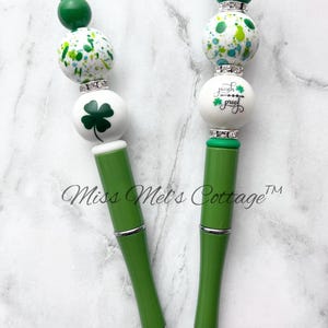 May include: Two green and white patterned pens with silver accents. The top of each pen has a green shamrock and the text "pinch proof" on one pen.