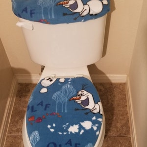 May include: A white toilet bowl with a blue and white Olaf themed toilet seat cover and lid cover. The cover features Olaf from the movie Frozen.