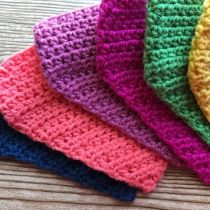 May include: A set of seven crocheted squares in various colors, including blue, pink, purple, green, and yellow. The squares are arranged in a rainbow pattern, with the blue square at the bottom and the yellow square at the top.