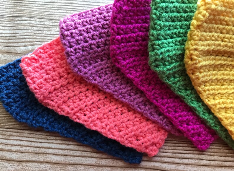 May include: A set of seven crocheted squares in various colors, including blue, pink, purple, green, and yellow. The squares are arranged in a rainbow pattern, with the blue square at the bottom and the yellow square at the top.