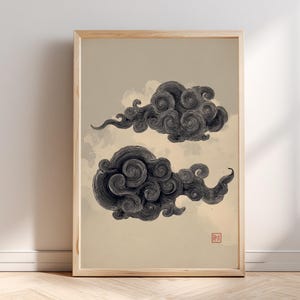 May include: Framed art print featuring two stylized, dark gray cloud formations against a beige background. The clouds have a swirling, textured appearance, with a small red stamp in the lower right corner. The artwork is encased in a light-colored wooden frame.