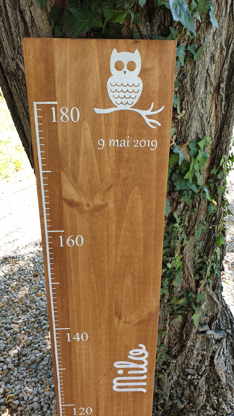 May include: A wooden height chart featuring a white owl design and a measurement scale. The chart shows measurements up to 180 cm, with the name "Milo" and the date "9 mai 2019" in white lettering.