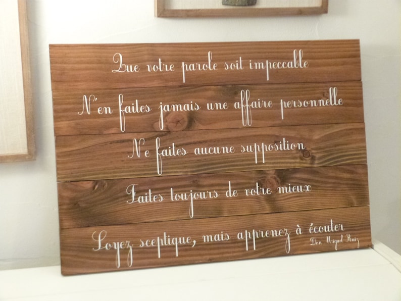 May include: A wooden sign with white lettering that reads: "Que votre parole soit impeccable. N'en faites jamais une affaire personnelle. Ne faites aucune supposition. Laites toujours de votre mieux. Loyez sceptique, mais apprenez &agrave; &eacute;couter. - Don Miguel Ruiz"