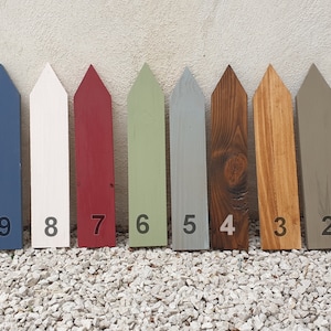 May include: Eleven painted wooden fence post markers in various colours. The colours include light blue, yellow, navy, white, red, green, grey, brown, tan, and dark grey. Each post is numbered from 1 to 11.