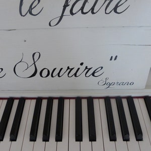 May include: White piano with black keys and the inscription "On le fait le sourire" in black cursive lettering. The inscription "Soprano" is also visible in black cursive lettering.