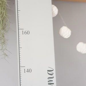 May include: A white wooden height chart with a grey elephant holding a heart-shaped balloon. The chart measures up to 180 cm and has the name "Emma" in cursive. A decorative item for a child's room.