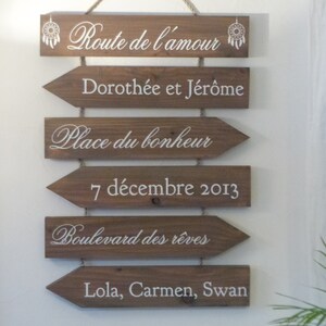 May include: Wooden sign with arrows pointing to the right, with the text "Route de l'amour", "Doroth&eacute;e et J&eacute;r&ocirc;me", "Place du bonheur", "7 d&eacute;cembre 2013", "Boulevard des r&ecirc;ves", and "Lola, Carmen, Swan".