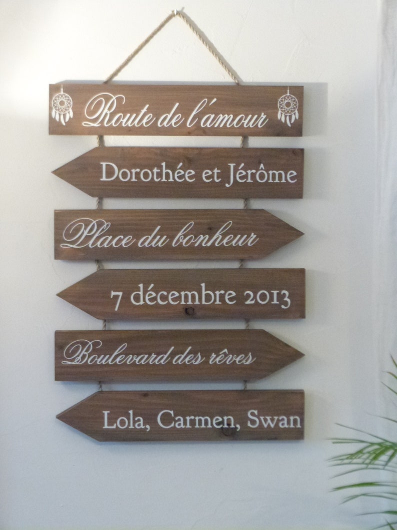 May include: Wooden sign with arrows pointing to the right, with the text "Route de l'amour", "Doroth&eacute;e et J&eacute;r&ocirc;me", "Place du bonheur", "7 d&eacute;cembre 2013", "Boulevard des r&ecirc;ves", and "Lola, Carmen, Swan".