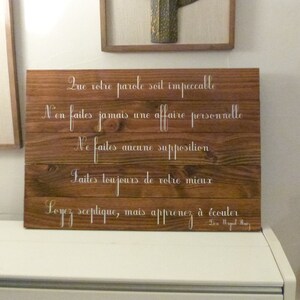 May include: A wooden sign with a white inscription in French. The text reads: "Que votre parole soit impeccable. N'en faites jamais une affaire personnelle. Ne faites aucune supposition. Faites toujours de votre mieux. Soyez sceptique, mais apprenez &agrave; &eacute;couter." The sign is on a white surface.