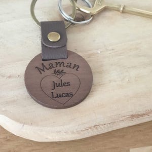 May include: A wooden keychain with the word "Maman" and the names "Jules" and "Lucas" engraved on it. The keychain has a brown leather strap and a metal ring. A brass key is also visible.