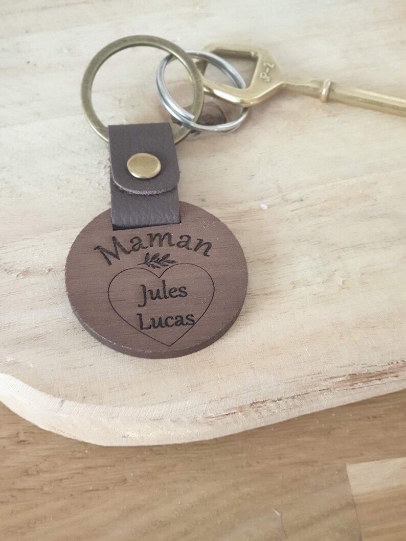 May include: A wooden keychain with the word "Maman" and the names "Jules" and "Lucas" engraved on it. The keychain has a brown leather strap and a metal ring. A brass key is also visible.