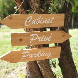 May include: Three wooden arrow signs hanging from a tree branch. The signs point to the right and are labeled "Cabinet", "Priv&eacute;", and "Parking" in white cursive lettering.