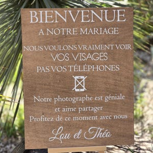Peut inclure: Panneau en bois avec texte blanc sur un petit chevalet en bois. Le panneau indique "BIENVENUE A NOTRE MARIAGE" et d'autres textes en français. Le panneau est marron avec des lettres blanches et est à l'extérieur.