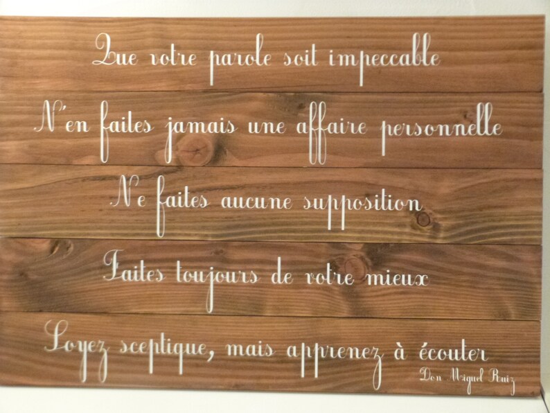 May include: Wooden sign with five white painted lines of text. The text reads: "Que votre parole soit impeccable. N'en faites jamais une affaire personnelle. Ne faites aucune supposition. Faites toujours de votre mieux. Soyez sceptique, mais apprenez &agrave; &eacute;couter. Don Miguel Ruiz."
