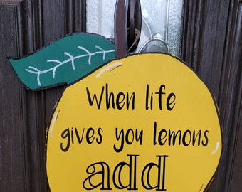 May include: A yellow lemon-shaped wooden sign with green leaves. The sign says "When life gives you lemons add vodka".
