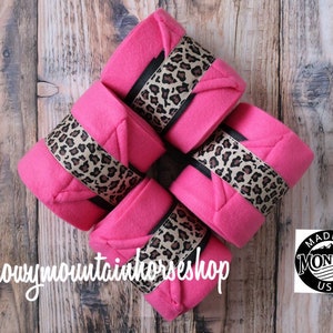May include: Four pink horse leg wraps with leopard print trim. The wraps are arranged in a square shape. The text "@snowymountainhorseshop" is visible in the bottom left corner of the image. A black and white logo with the text "MADE IN MONTANA USA" is visible in the bottom right corner of the image.