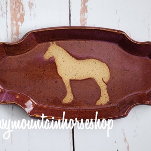 May include: A brown ceramic serving dish with a scalloped edge. The dish features a cutout silhouette of a horse in a light brown colour. The dish is made in Montana, USA.  @snowymountainhorseshop