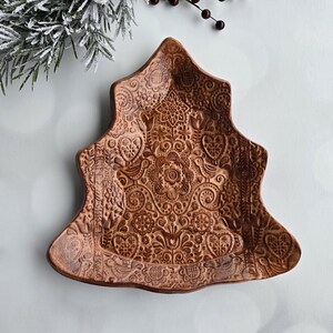 May include: A brown ceramic Christmas tree-shaped dish with an intricate floral and bird design.