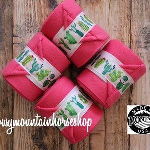 May include: Four pink horse leg wraps with white and green cactus print. The wraps are rolled up and arranged in a circle. The text "@snowymountainhorseshop" is visible in the bottom left corner. A black and white sticker with the text "MADE IN MONTANA USA" is visible in the bottom right corner.