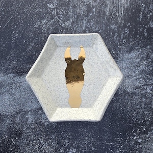 May include: A white ceramic hexagonal tray with a gold silhouette of a horse's head in the centre.