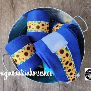 May include: Four blue horse leg wraps with sunflower print. The wraps are rolled up and sitting in a silver bucket. The wraps are made in Montana, USA.