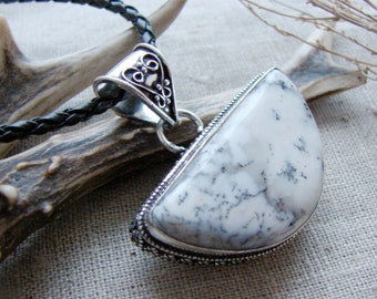 Puede incluir: Un colgante de ágata blanco y gris con una anilla de filigrana plateada, colgando de un cordón de cuero negro.