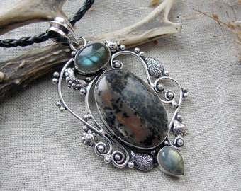 May include: A silver pendant featuring a large oval brown and black mottled stone in the center, flanked by a smaller oval labradorite stone at the top and a teardrop-shaped labradorite stone at the bottom, all set in an ornate silver frame.