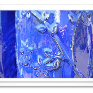 May include: Close-up of a blue ceramic surface with a raised floral design. The surface is glossy and reflects light.