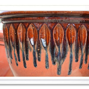 May include: Close-up of a terracotta pot with a brown and black glaze. The pot has a decorative design of leaf-like shapes.