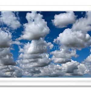 May include: A framed print featuring a vibrant blue sky filled with fluffy, white cumulus clouds. The clouds are densely packed, creating a dynamic and textured visual effect. The artwork is presented in a white frame.