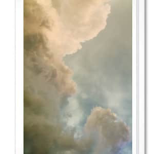 May include: A photograph of a cloudy sky with a large, fluffy cloud in the upper left corner and smaller, wispy clouds in the lower right corner. The sky is a light blue color, and the clouds are a soft, white color.