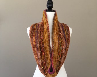 May include: A knitted cowl with a textured pattern in shades of brown, orange, and purple. The cowl is displayed on a white mannequin.