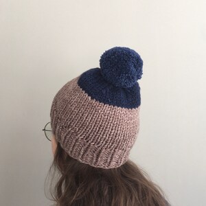 May include: A brown and navy blue knitted beanie with a navy blue pom pom on top.
