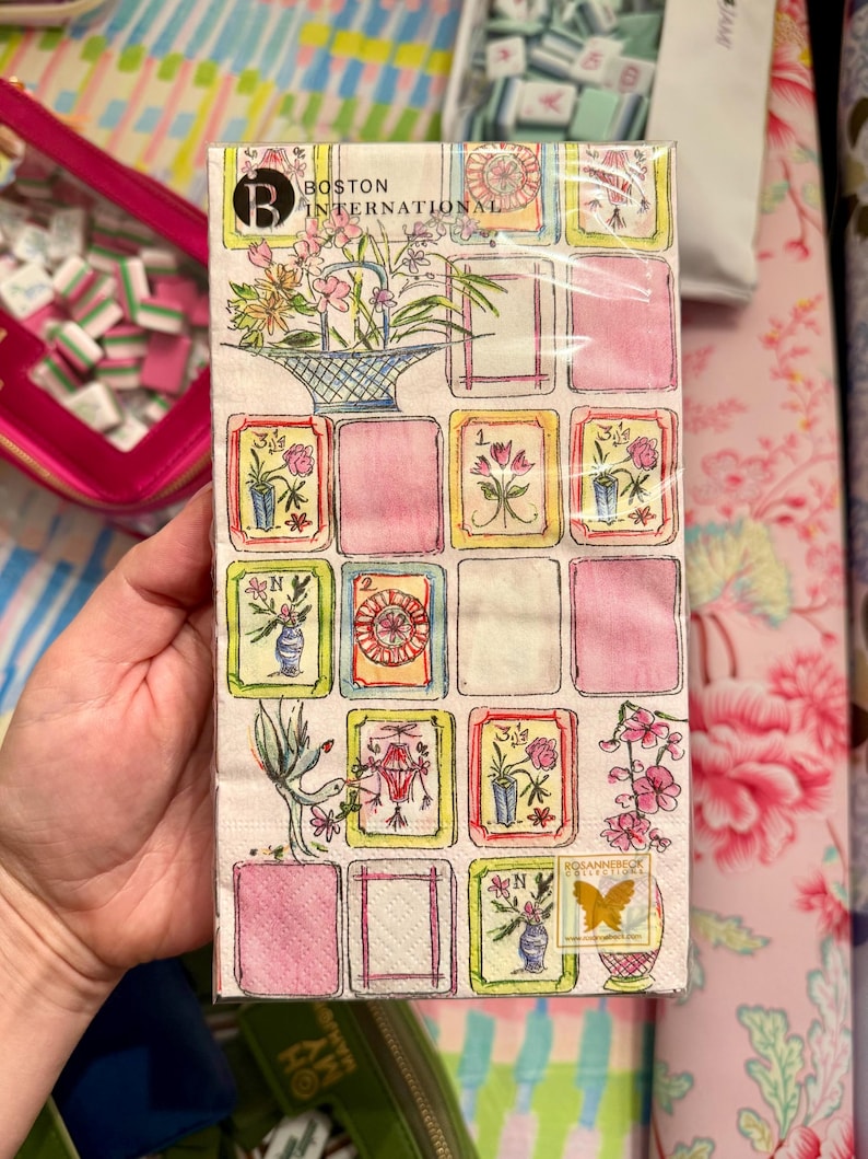 K&ouml;nnte beinhalten: Eine Packung dekorativer Papierservietten mit floralem und botanischem Design. Die Servietten haben ein Rastermuster mit rosa Quadraten und Aquarellillustrationen von Blumen, Vasen und V&ouml;geln. Der Text "BOSTON INTERNATIONAL" ist sichtbar.