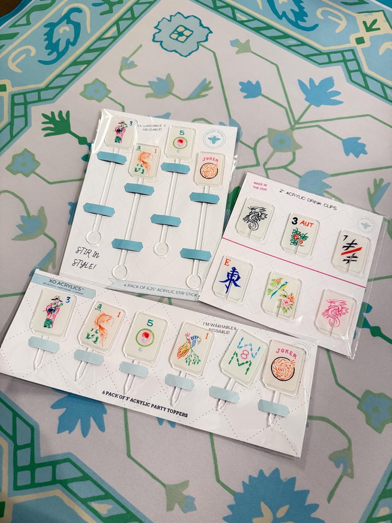 May include: Three sets of clear acrylic drink accessories in plastic packaging. One set contains four 6.25-inch stir sticks, one set contains six 3-inch party toppers, and one set contains two drink clips, all featuring colorful mahjong tile designs.