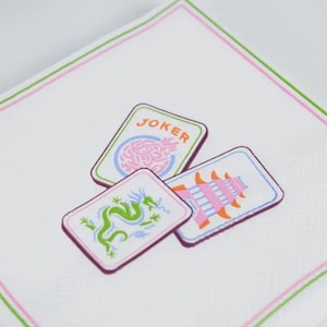 K&ouml;nnte beinhalten: Wei&szlig;es Taschentuch mit rosa und gr&uuml;nem Rand, das drei Spielkarten zeigt. Die Karten zeigen einen Drachen, eine Pagode und ein Gehirn mit dem Wort "JOKER". Das Design ist in Rosa-, Gr&uuml;n- und Blaut&ouml;nen gehalten.