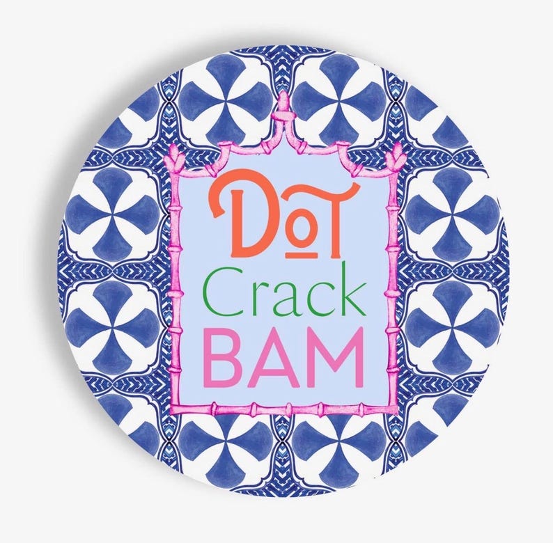 May include: A circular decorative plate featuring a blue and white geometric tile pattern. In the center, a light blue rectangular panel is framed by a pink bamboo-style border, displaying the text "DoT Crack BAM" in orange, green, and pink.