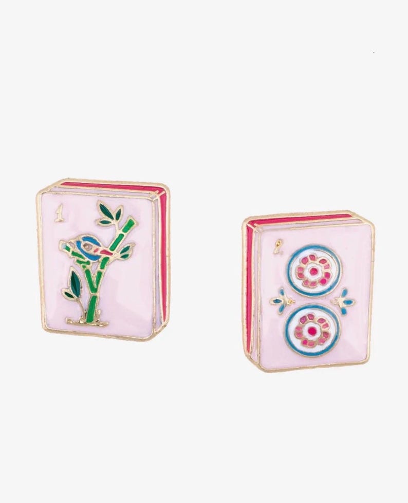 May include: Two pink Mahjong tile-shaped earrings. One earring features a bird on a bamboo branch, the other has two flower designs. Both have gold trim and red edges. The earrings are set against a white background.