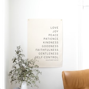 May include: A beige canvas print with black text listing the fruits of the spirit: love, joy, peace, patience, kindness, goodness, faithfulness, gentleness, and self-control. The text also includes the scripture reference Galatians 5:22-23.