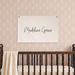 Nursery name banner canvas flag with baby girl's name in cursive script on cream canvas with grommets