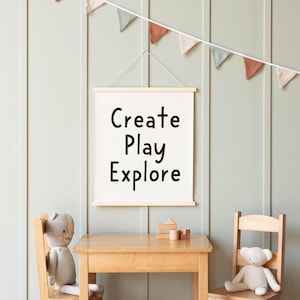 May include: A white framed canvas with the text "Create Play Explore" hanging on a light green wall. Two wooden chairs with stuffed animal toys are in front of a wooden table with wooden blocks on it.