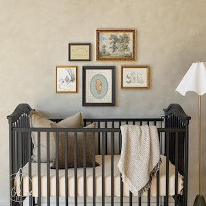 May include: A dark grey cot with a beige mattress, cushions, and a fringed blanket. Above the cot, framed artwork includes a Winnie the Pooh print and landscape paintings. A floor lamp with a white shade is on the right.