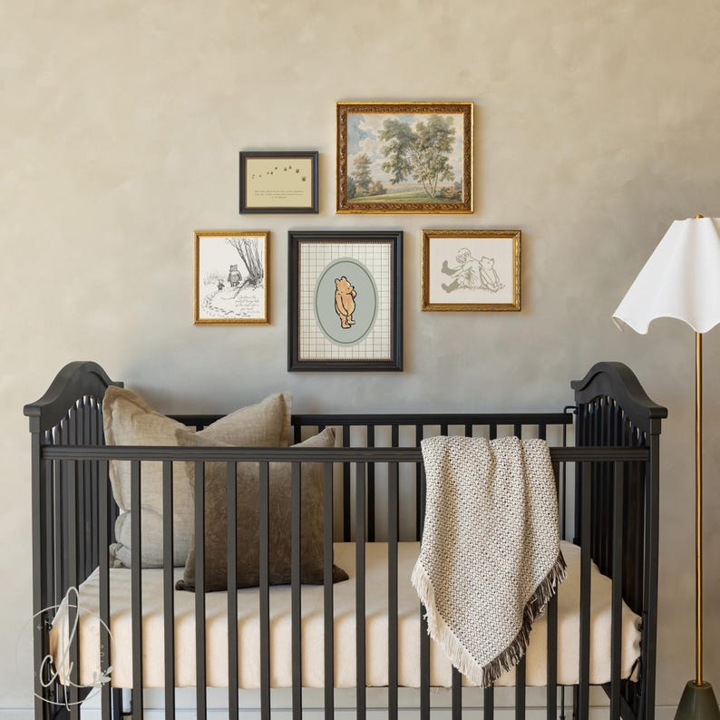 May include: A dark grey cot with a beige mattress, cushions, and a fringed blanket. Above the cot, framed artwork includes a Winnie the Pooh print and landscape paintings. A floor lamp with a white shade is on the right.