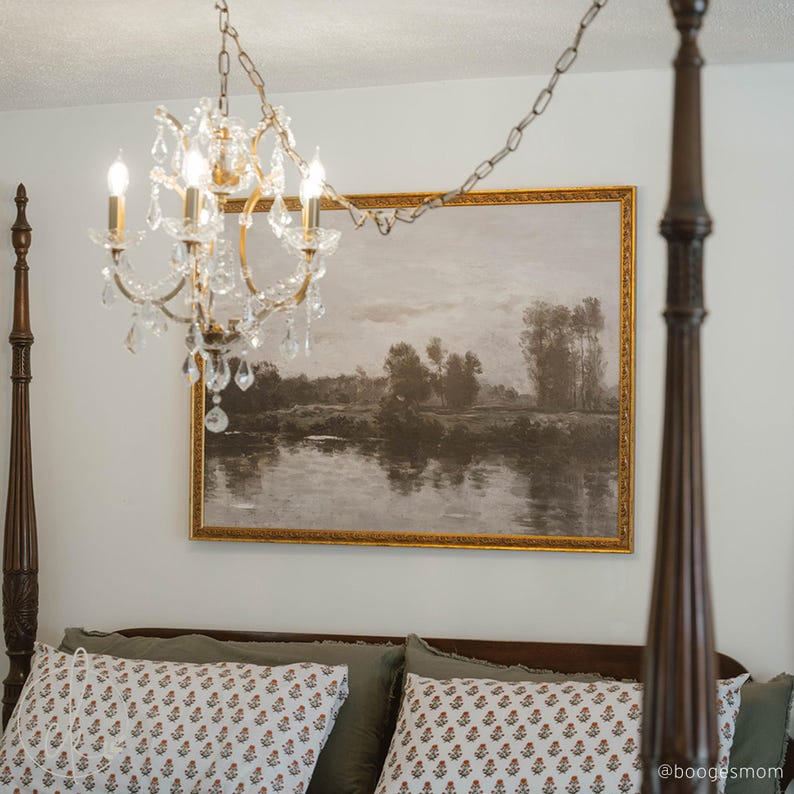 May include: A crystal chandelier with four lights hangs above a bed. A landscape painting with a gold frame is mounted on the wall. The bed has decorative pillows and a dark wooden frame.
