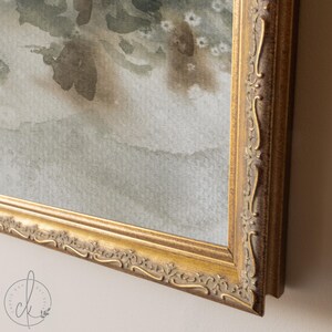 May include: A framed watercolor painting with a gold ornate frame. The artwork features soft, muted tones of green, gray, and brown, suggesting a landscape or abstract floral design. The frame has detailed carvings.