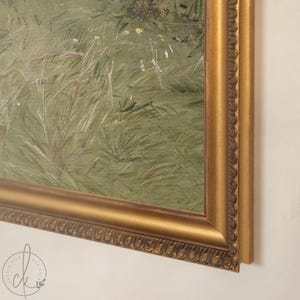 May include: A framed oil painting depicting a field of tall green grass with small white and yellow wildflowers. The artwork is enclosed in a decorative, ornate gold-colored frame with a textured, beaded edge detail along the inner border.