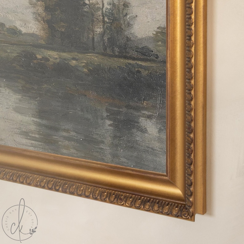 May include: An antique landscape painting in a gold ornate frame. The artwork depicts a river scene with trees and a cloudy sky. The frame has a detailed, textured design. The painting is a vintage piece.