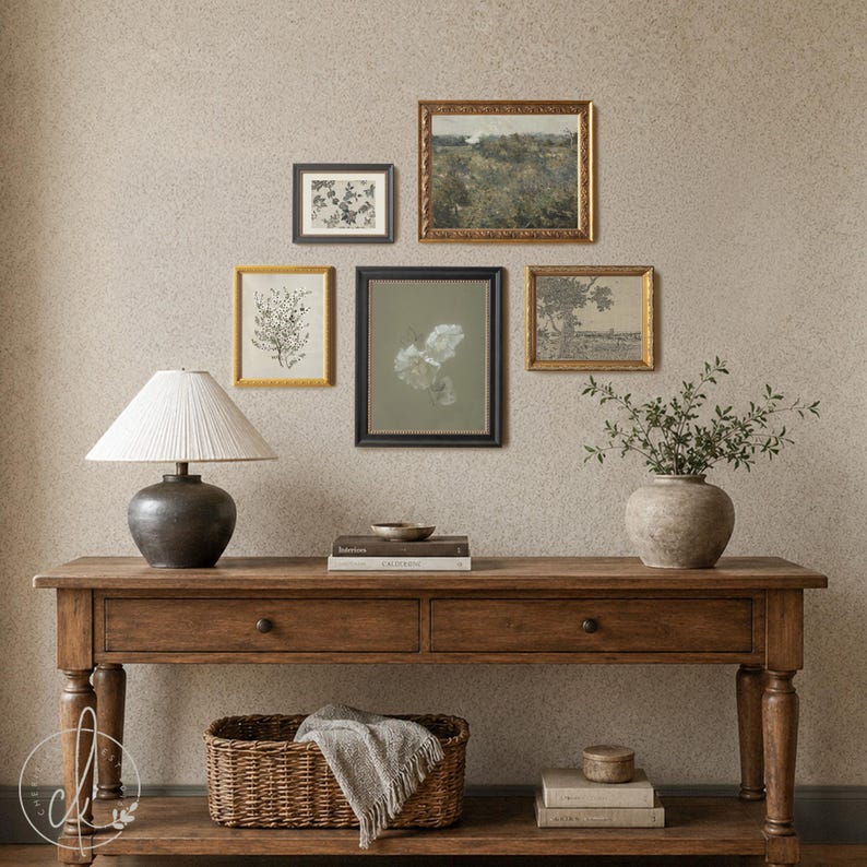 May include: A wooden console table with two drawers and a lower shelf, featuring a table lamp with a pleated shade, a ceramic vase with greenery, a woven basket with a textile, stacked books, and five framed wall art pieces in various sizes.